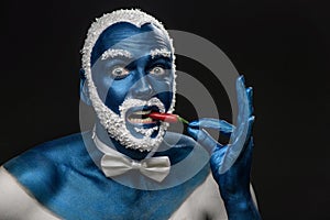 Man painted in blue color with snowy hair and beard eating chili pepper