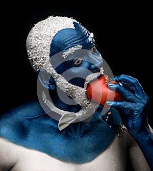 Man painted in blue color with snowy hair and beard eating tomato