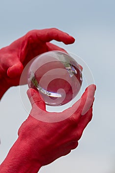 Man with painted red hands passes glass sphere between hands