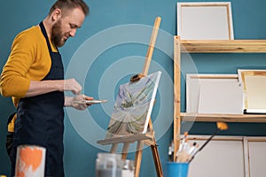 Man painter standing in front of the canvas and drawing. Artist using oil paints, artist brushes, canvas and frame