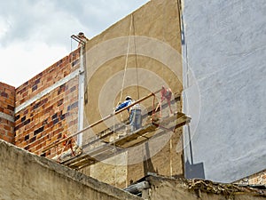 A man painting a big wall from a rustic and poorly secure hanging scaffold