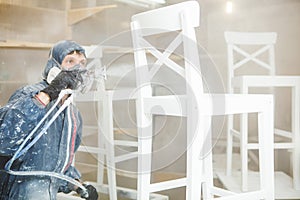 Man painting chair into white paint in respiratory mask. Application of flame retardant ensuring fire protection