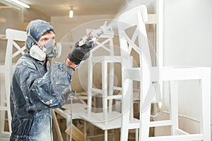 Man painting chair into white paint in respiratory mask. Application of flame retardant ensuring fire protection