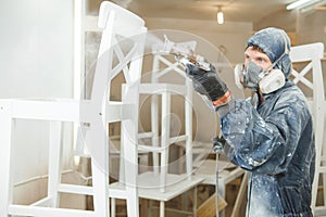 Man painting chair into white paint in respiratory mask. Application of flame retardant ensuring fire protection
