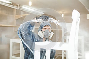 Man painting chair into white paint in respiratory mask. Application of flame retardant ensuring fire protection photo