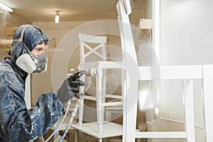 Man painting chair into white paint in respiratory mask. Application of flame retardant ensuring fire protection photo