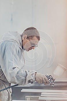 Man painting furniture details. Worker using spray gun.