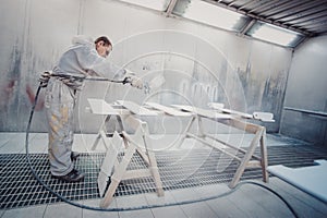 Man painting furniture details. Worker using spray gun.