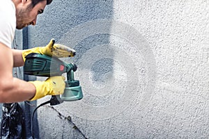 Man painting a grey wall, renovating exterior walls of new house photo