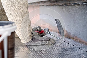 Man painting home socle with paint roller. Close up of rolling grey paint on building plinth. Home renovation