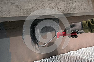 Man painting home socle with paint roller. Close up of rolling grey paint on building plinth. Home renovation