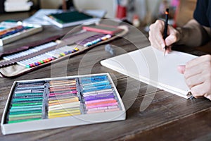 Man painting with pencil and pastel crayon chalks on paper. box of pastel chalks and color pencils on the wooden table