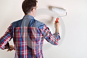 Man painting with roller a white wall behind detail