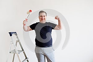 The man is painting the wall and having fun. The man jokingly shows his muscles and strength during repairs.