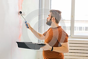 Man painting wall with paint roller - renovation and redecoration concept