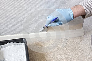 Man painting wall using paintbrush.  Cutting in skirting board