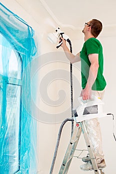 Man painting walls with paint spray gun