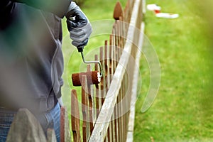 Man is painting wooden fence with brown paint outside