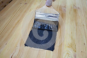 A man paints with black paint on a wooden surface