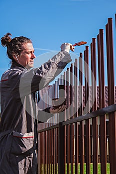 A man paints an iron fence in the garden and listens music in headphone.