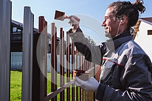 A man paints an iron fence in the garden and listens music in headphone.