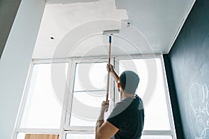 Man paints the walls and the ceiling in gray color, standing with his back to the camera. Focus on the roller.