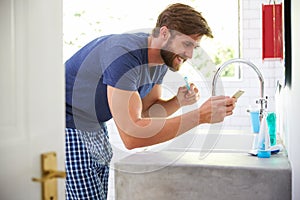 Man In Pajamas Brushing Teeth And Using Mobile Phone