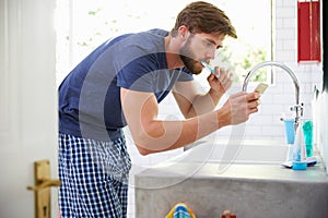 Man In Pajamas Brushing Teeth And Using Mobile Phone