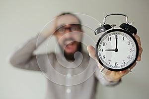 Man in panic holds alarm clock and head in fear of deadline