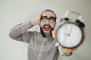 Man in panic holds alarm clock and head in fear of deadline