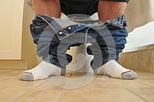 Man with pants down sitting at the toilet