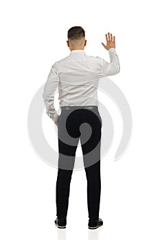 Man in pantsuit and white shirt is standing with hand raised. Rear view. Isolated