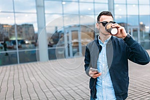 A man with a paper Cup of coffee, goes through the city, a handsome guy in stylish clothes and sunglasses, making a phone call