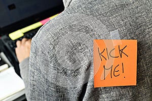 Man with a paper with the text kick me attached to his back photo