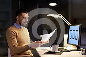 Man with papers and computer works at night office