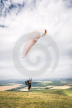A man paraglider taking off from the edge of the mountain with fields in the background. Paragliding sports