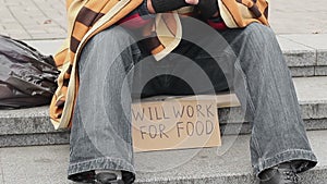 Man in park with ready to work for food sign, homeless begging, poverty, sadness