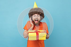 Man in party cone holding his birthday present, being surprised, yelling.