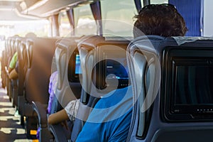 The man on the passenger seat of the bus listens to music and looks at the tablet. He looks at the device`s screen and smiles