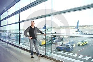 Man, a passenger, waiting for his flight, stands at the window and looks at the airport runway, a travel concert