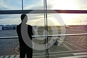 Man, a passenger, waiting for his flight, stands at the window and looks at the airport runway, a travel concert