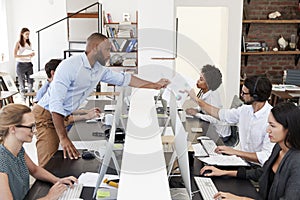 Man passing document across desk at a busy open plan office