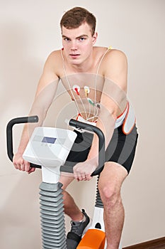 Man patient, pedaling on a bicycle ergometer stress test system for the function of heart checked. Athlete does a