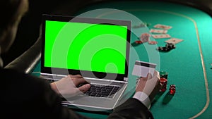 Man paying poker bet with credit card, using laptop green screen, online winning