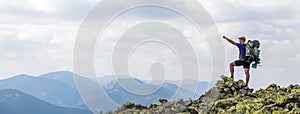 Man on peak of mountain. Emotional scene. Young man with backpack standing with raised hands on top of a mountain and enjoying mo