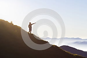Man on peak of mountain. Emotional scene. Young man with backpack standing with raised hands on top of a mountain and enjoying mo