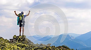 Man on peak of mountain. Emotional scene. Young man with backpack standing with raised hands on top of a mountain and enjoying mo