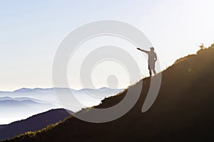 Man on peak of mountain. Emotional scene. Young man with backpack standing with raised hands on top of a mountain and enjoying mo