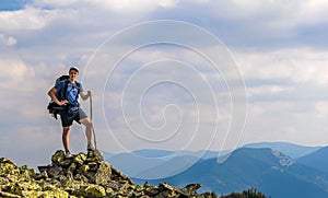 Man on peak of mountain. Emotional scene. Young man with backpack standing with raised hands on top of a mountain and enjoying mo