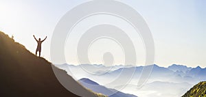 Man on peak of mountain. Emotional scene. Young man with backpack standing with raised hands on top of a mountain and enjoying mo